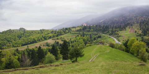 rural mountain landscape in spring. grassy hills and fields on rolling hills. distant ridge beneath...