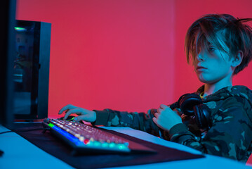 Portrait of  gamer boy playing video games on computer in dark room wearing headphones and using backlit colorful keyboard © stenkovlad