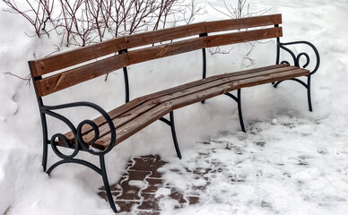 Bench made of metal and wood close-up on the background of snow in winter