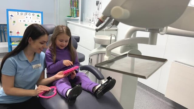 dental office children's dentistry the doctor plays with the girl on the dental chair gives her a pink box choose a ring so that child relaxes not be afraid of doctor's dentistry children's toys