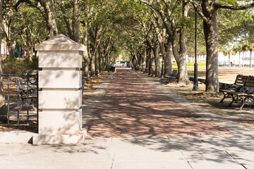 Pillar and tree-lined, shaded brick walkway in Charleston Riverfront Park on bright, sunny morning....