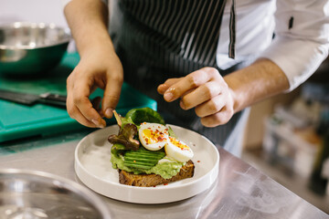 The chef is preparing food. Close-up of a male chef preparing avocado toast in a spacious modern kitchen.
