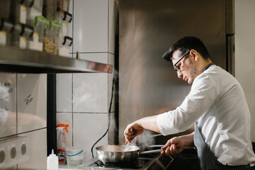 Сooking food, profession and people concept - male chef cook with frying pan at restaurant kitchen...