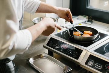 The concept of cooking, professions and people. Male chef frying carrot pancakes in restaurant kitchen..