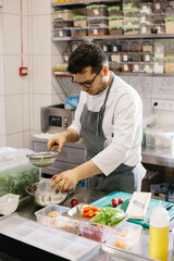 Preparing vegetables for a delicious bowl dish: a male chef in a contemporary restaurant kitchen.