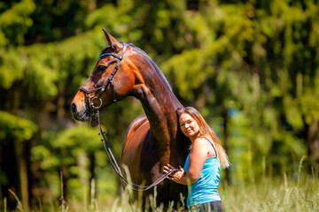Horse stands with a young woman in a meadow, horse looks attentively to the right and the woman...