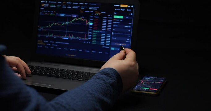 The broker trades on the cryptocurrency exchange. The broker spins a bitcoin coin in his hand and monitors the cryptocurrency chart on the stock exchange. Cryptocurrency trading concept.
