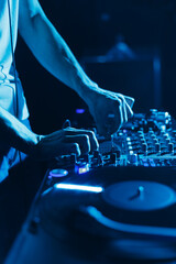 Club DJ mixing vinyl records in blue stage lights. Close up photo of disc jockey playing music on party in night club