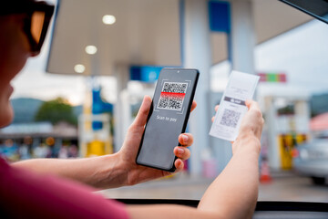 Woman using contactless payment by mobile phone with QR code at car filling station