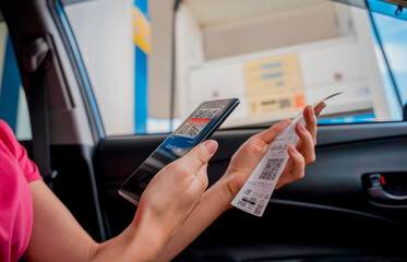 Woman using contactless payment by mobile phone with QR code at car filling station