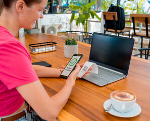 Woman using contactless payment by mobile phone with QR code at cafe