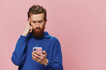 Portrait of a man with a phone in his hands doing looking at it and talking on the phone, on a pink background. Communicating online social media, lifestyle