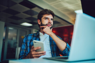 Thoughtful man sitting with laptop and smartphone at table