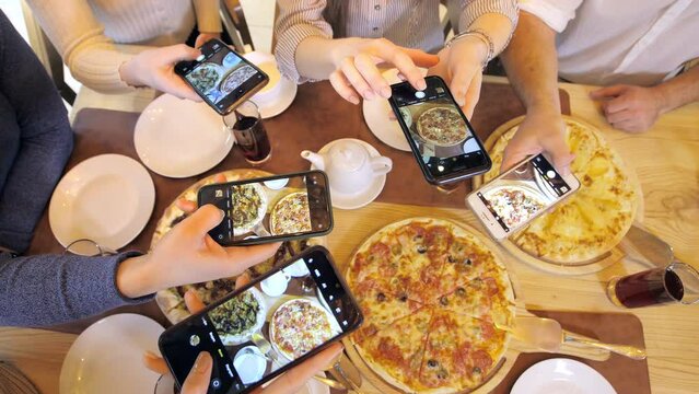 A happy group of friends are sitting at a table in a cozy restaurant, laughing and having fun. Friends together in a cafe take photos and videos of food for social networks. Pizzeria.Selfies with food