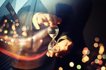 Close up of a businessman holding hourglass. Office. Morning cityscape. Concept of time management....