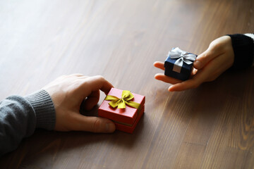 Top view of male and female hands holding gift box with ribbon on wooden background. Present for birthday, valentine day, Christmas, New Year. Congratulations background copy space.