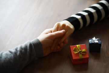 Top view of male and female hands holding gift box with ribbon on wooden background. Present for...