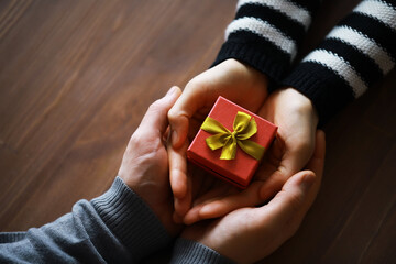 Top view of male and female hands holding gift box with ribbon on wooden background. Present for...