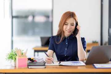 Fototapeta na wymiar Cheerful business Asian woman freelancer making telephone call share good news about project working in office workplace, business finance concept. 