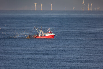 Obraz premium A cutter with lifted drag nets on the North sea with wind turbines in the background