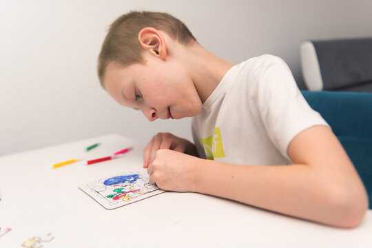 A boy of 4-7 years old sits at the table and draws with multi-colored paints. Children's creativity. Children's hobbies
