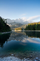 Fototapeta na wymiar Spiegelung von Bergen mit Wolken im morgendlichen Licht in See. Zugspitze und Eibsee in Bayern.