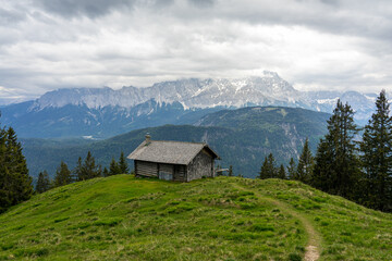 Fototapeta na wymiar Hütte auf Almwiese in den Vergen mit Pfad oder Weg und Bergpanorama.