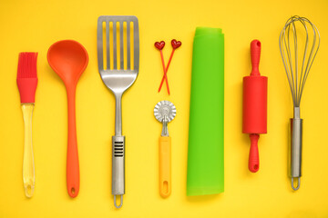 culinary background, culinary accessories on a yellow background - slotted spoon, dough knife, spatula, whisk, brush, skewers, silicone mat, rolling pin, ladle