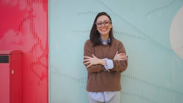Happy woman in glasses snapping his fingers standing outdoor near colorful wall smile and talking something. Positive female fix hair laught an tel a story 