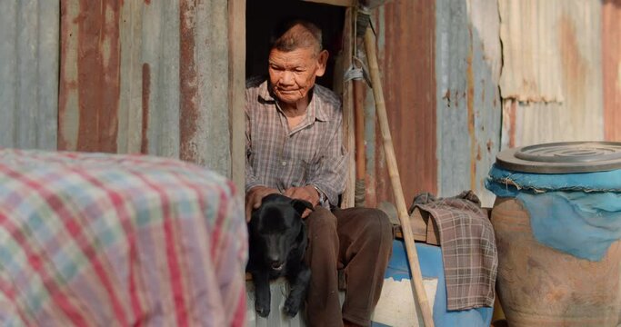 Asian farmer who is an elderly, poor, lonely person working as a farmer sitting on a narrow window Of the old house, like his hand, rubbed his dog's head in the morning.