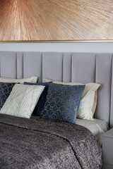 Close-up of a new blue and gray bed with decorative pillows, fabric headboard in a bedroom in a staged model of a hotel or apartment. 