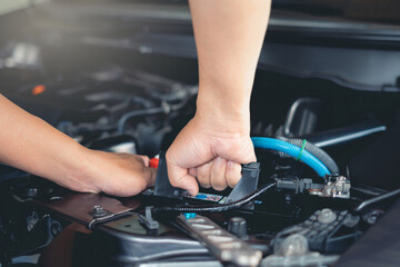 Close-up hand of a car mechanic in a service center picking up a new battery to replace the car in...