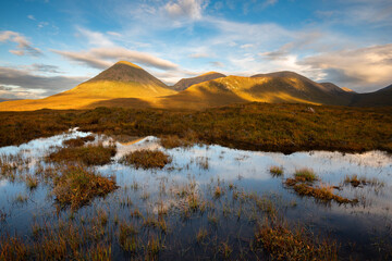 Red Cuillins covered in golden light seen from boggy moorland near Sligachan. Isle of Skye,...