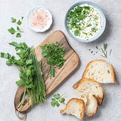 Butter with fresh herbs: wild onion, parsley, rosemary and pink salt on a wooden board, gray stone background, rustic style. Simple and healthy snacks and aperitif, artisan bread, square crop