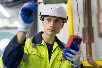 Male electrical engineer using digital multimeter checking voltage on robot arm welding machine at...