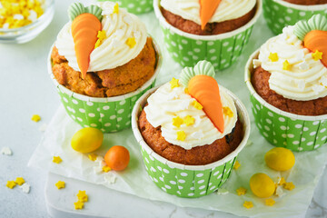 Carrot cake cupcakes for Easter. Carrot cupcakes with cream cheese frosting decorated with tiny marzipan carrots on white background. Happy Easter and spring holiday concept. Holydays homemade dessert