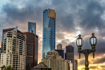 The sun sets over the city of Melbourne. An old fashioned lamppost in the foreground with ta modern...