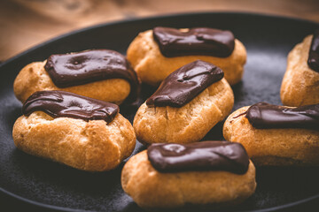 Mini eclairs with dark chocolate on a black plate, french pastry specialty with custard cream