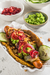 Healthy vegetarian hot dog with flatbread made from vegetables, topped with red onions, pickles and pea puree, white background