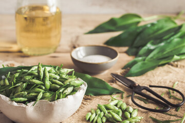 Wild garlic buds and leaves, salt and vinegar on a rustic wooden background