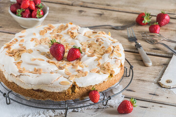 Rhubarb pie with meringue topping and fresh strawberries on a cooling rack on a rustic wooden table