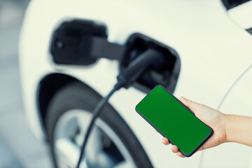 Mockup phone with green screen display energy status of electric vehicle connected to charging...