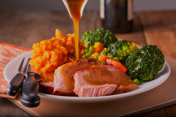 Gammon roast dinner with gravy being poured over it in a rustic setting.