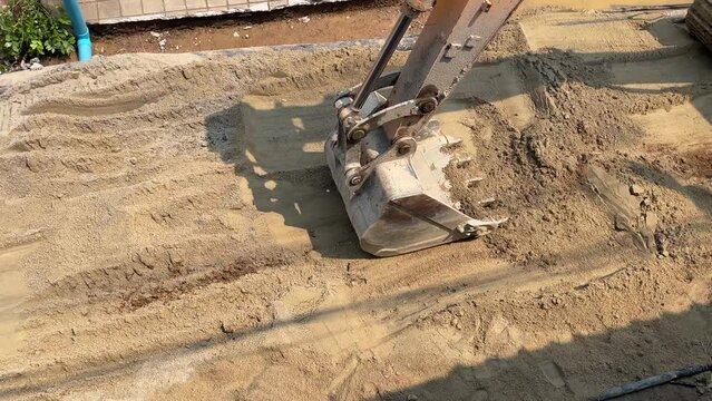 Top view excavator truck bucket level the sand on soil ground at construction site outdoor sunny day near residential area street before pouring concrete cement, Thailand