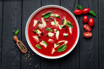 Summer cold tomato vegetable soup Gazpacho with mozzarella cheese on the black table. Vegetarian cuisine.