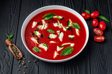 Summer cold tomato vegetable soup Gazpacho with mozzarella cheese on the black table. Vegetarian cuisine.