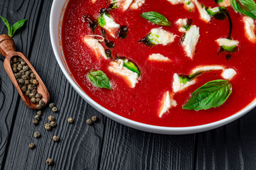 Summer cold tomato vegetable soup Gazpacho with mozzarella cheese on the black table. Vegetarian cuisine.