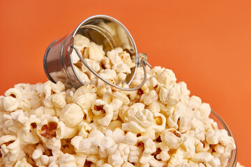 A bowl on an orange background is completely filled with popcorn.