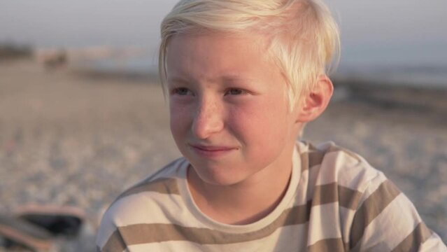 Close-up, a handsome blond boy squinting at the setting sun on the beach