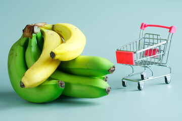 Variety of yellow and green bananas next to a miniature supermarket cart. The concept of buying and...